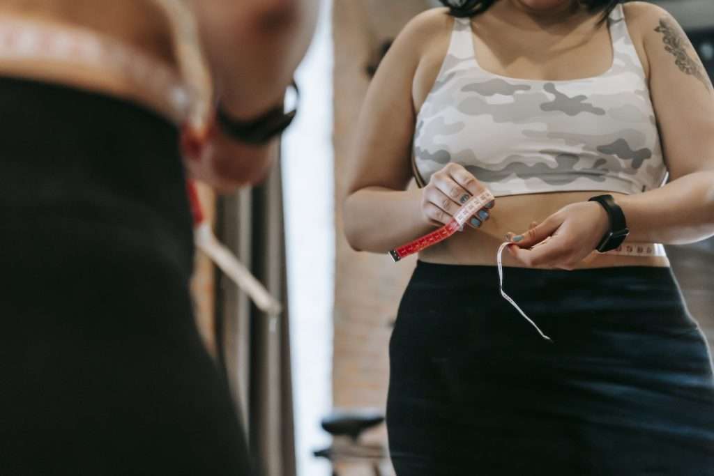 Woman measuring waist with tape in gym